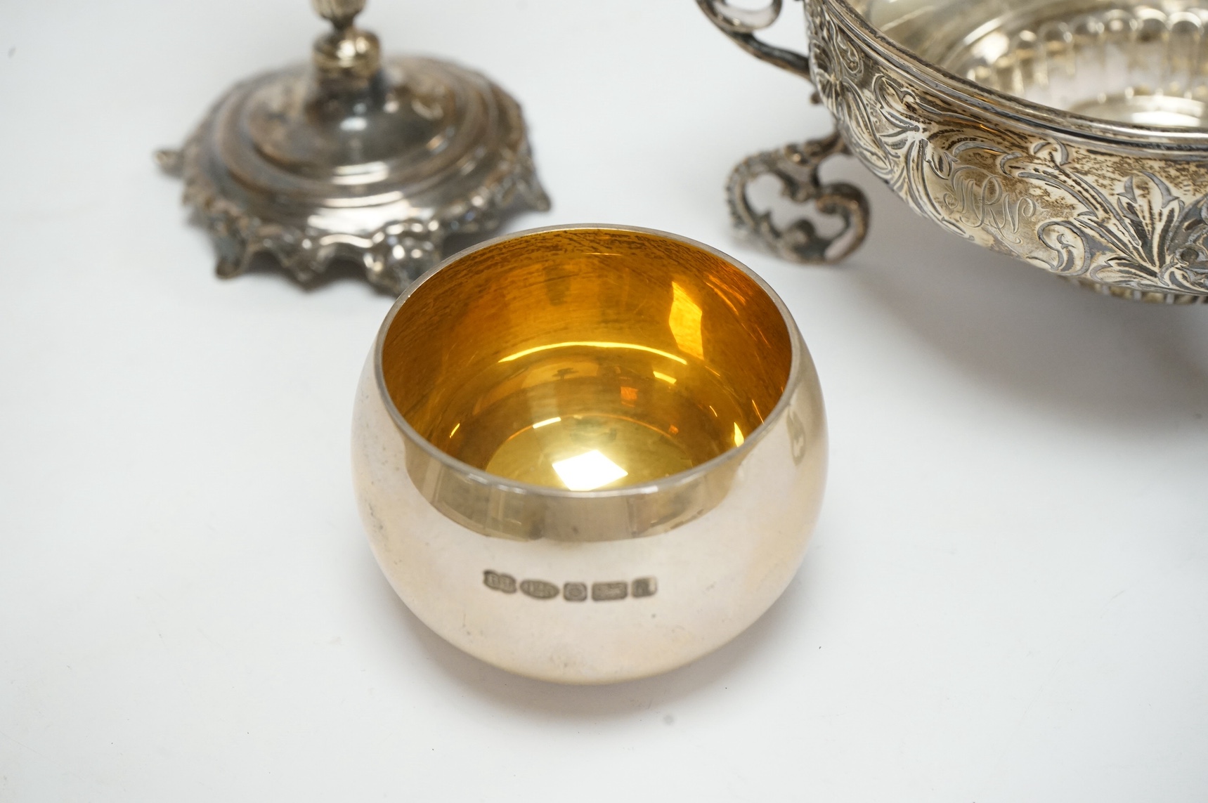 A late Victorian embossed silver bowl, on tripod supports, London, 1890, lacking glass insert?, diameter 12.2cm, together with a Middle Eastern white metal candlestick and a modern silver tumbler cup. Condition - fair to